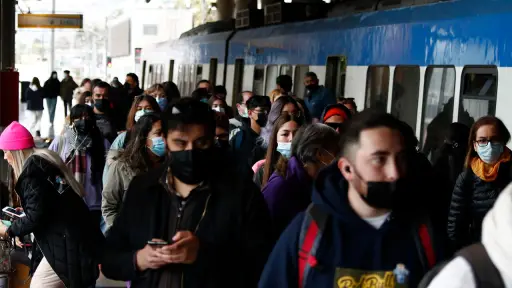 una multitud de personas de pie utilizando mascarillas junto a un tren