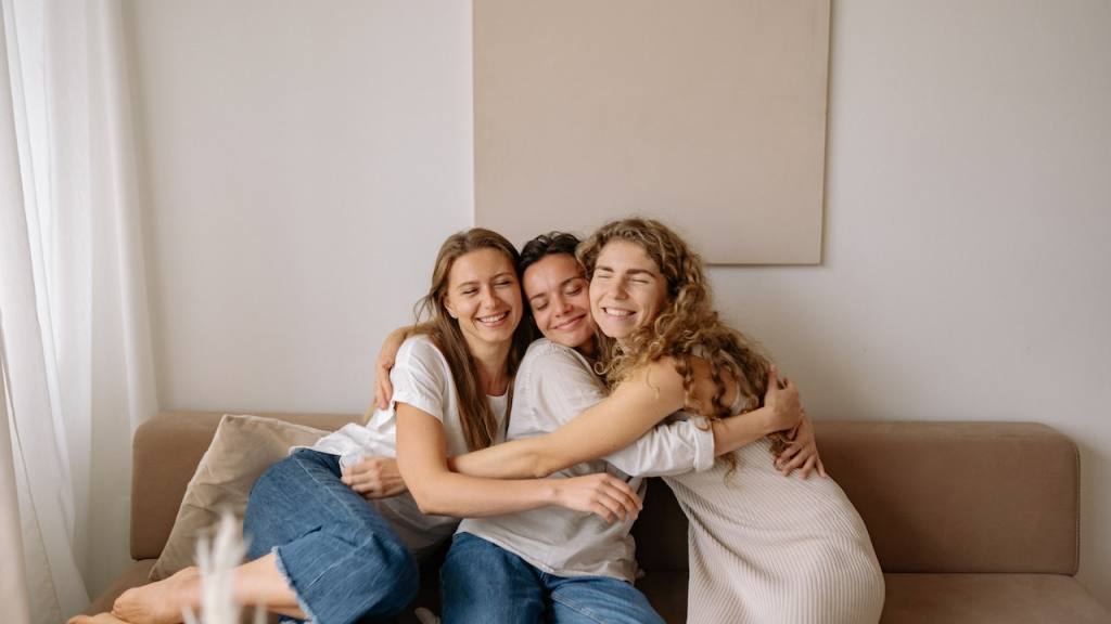 tres mujeres celebran su amistad abrazadas en un sillón café / 