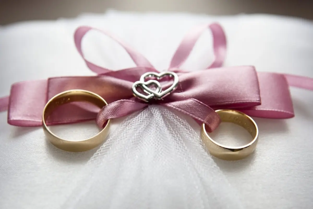 dos anillos de matrimonio de oro con una cinta rosa atada alrededor de ellos