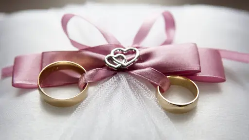 dos anillos de matrimonio de oro con una cinta rosa atada alrededor de ellos