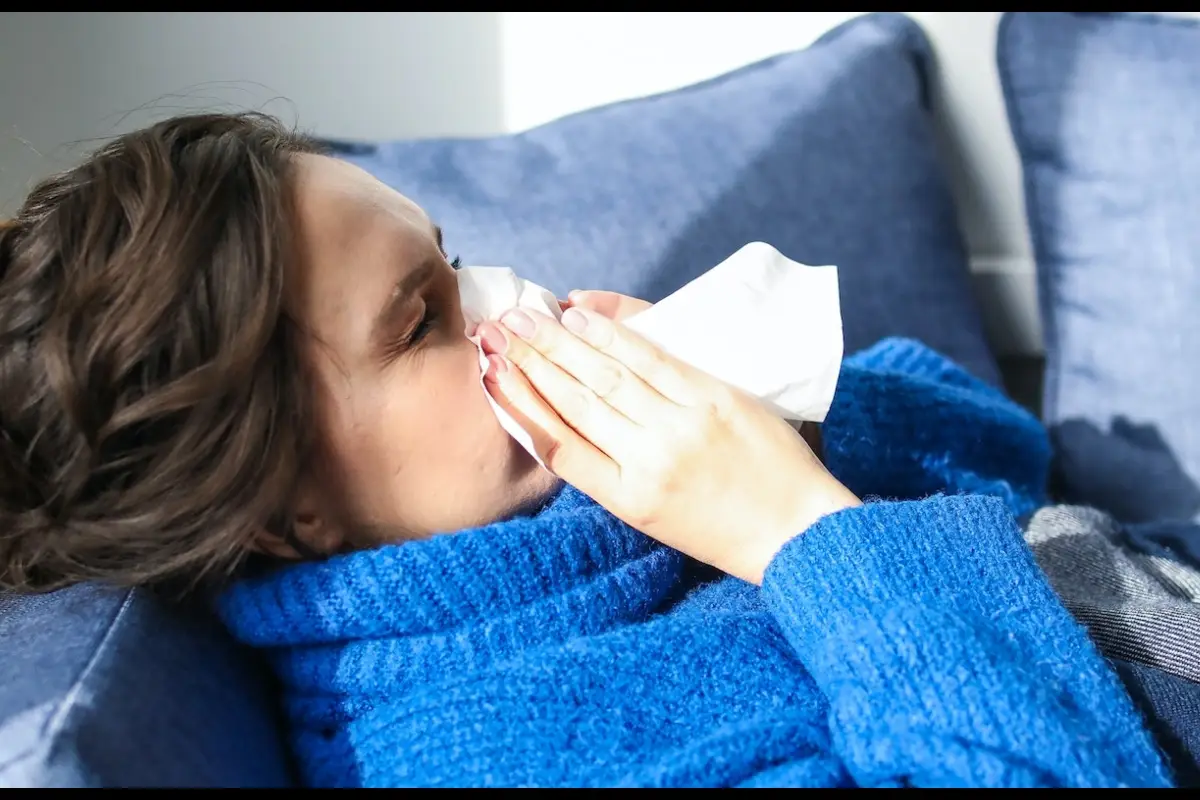 Una mujer estornuda mientras está sentada en un sofá debido a problemas de salud o falta de vitamina C