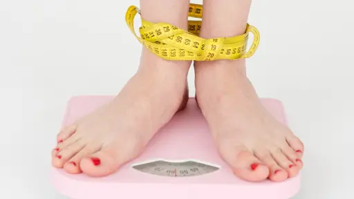 una mujer de pie sobre una balanza con una cinta métrica alrededor de los tobillos