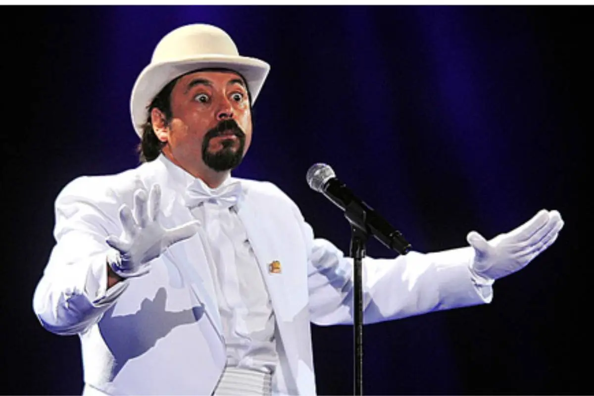 el humorista Bombo Fica de traje blanco y sombrero frente a un micrófono.