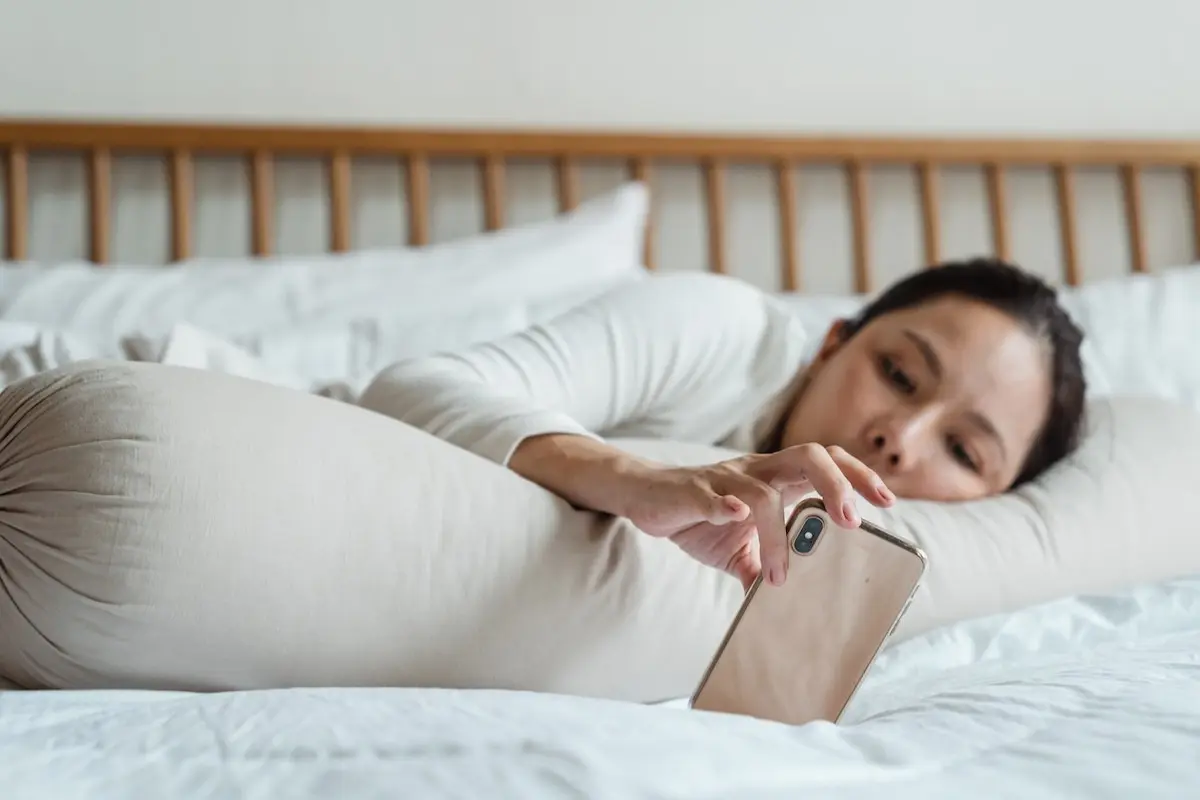 una mujer acostada en una cama sostiene su celular