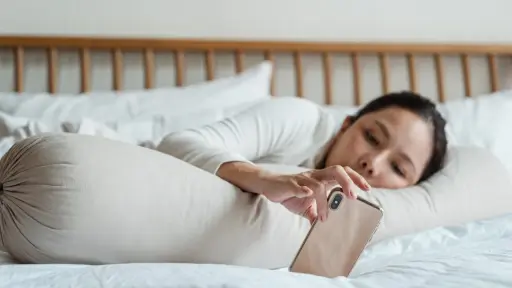 una mujer acostada en una cama sostiene su celular