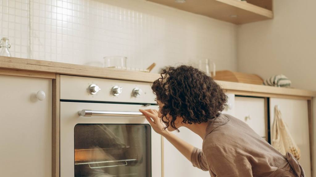 una mujer agachada observa el interior de su horno mientras cocina / 