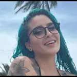 Carla Rose, con pelo verde y gafas, sonriendo en primer plano