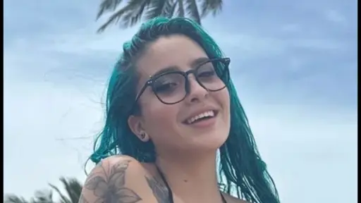 Carla Rose, con pelo verde y gafas, sonriendo en primer plano