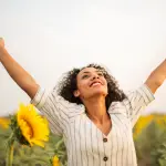 mujer con los brazos abiertos en posición de victoria, en un campo de girasoles, Julio