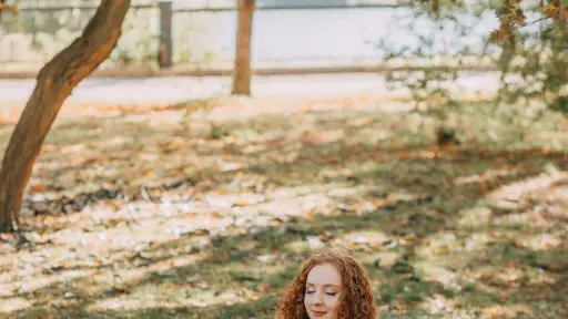 Mujer adulta sentada en el suelo en posición de meditación con las piernas cruzadas y las manos sobre las rodillas, tiene los ojos cerrados y expresa serenidad, practicando meditación mindfulness para reducir estrés y ansiedad e incrementar la claridad mental.