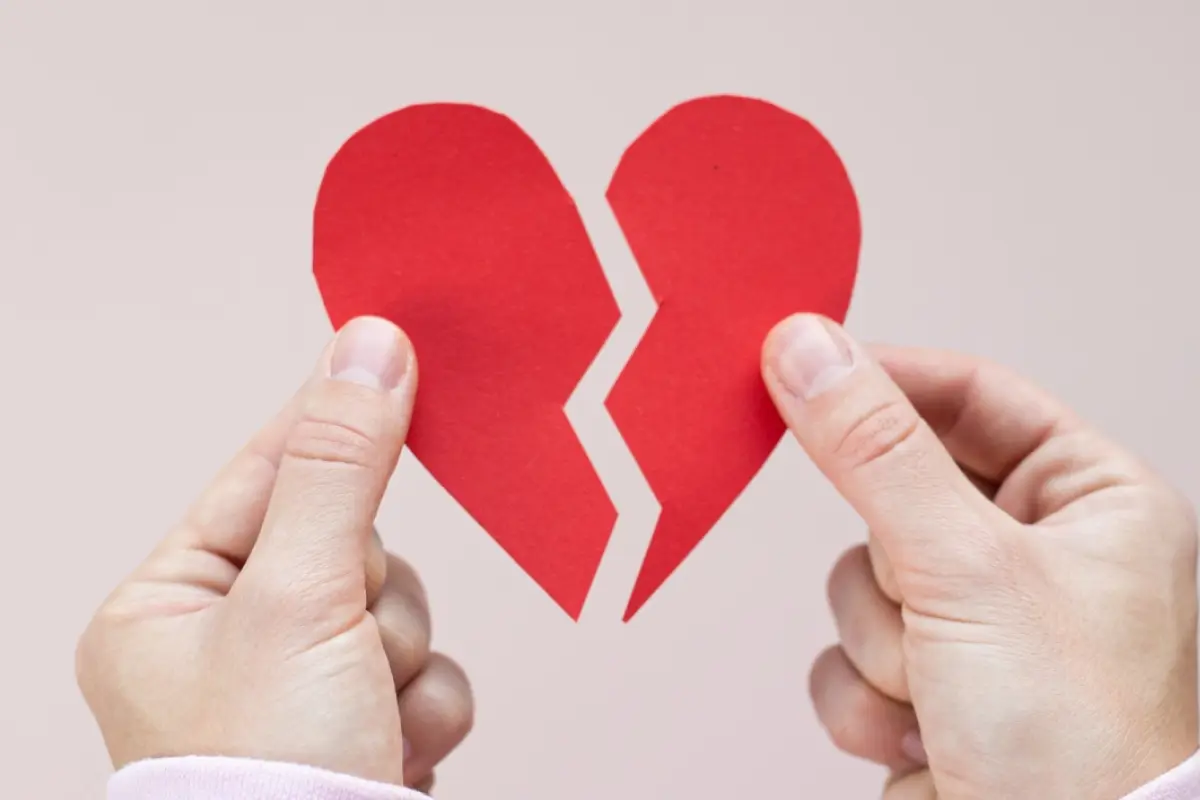 un corazón de papel partido a la mitad sostenido por dos manos en cada extremo