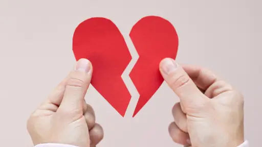 un corazón de papel partido a la mitad sostenido por dos manos en cada extremo
