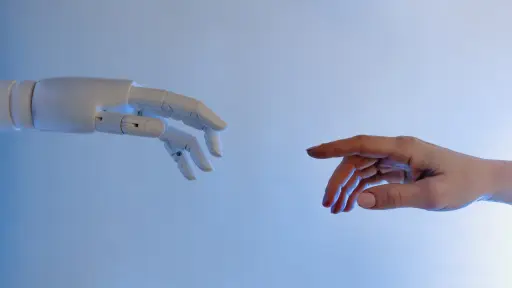 una mano robótica y una mano humana encontrándose en el centro de la foto tocando sus dedos índice