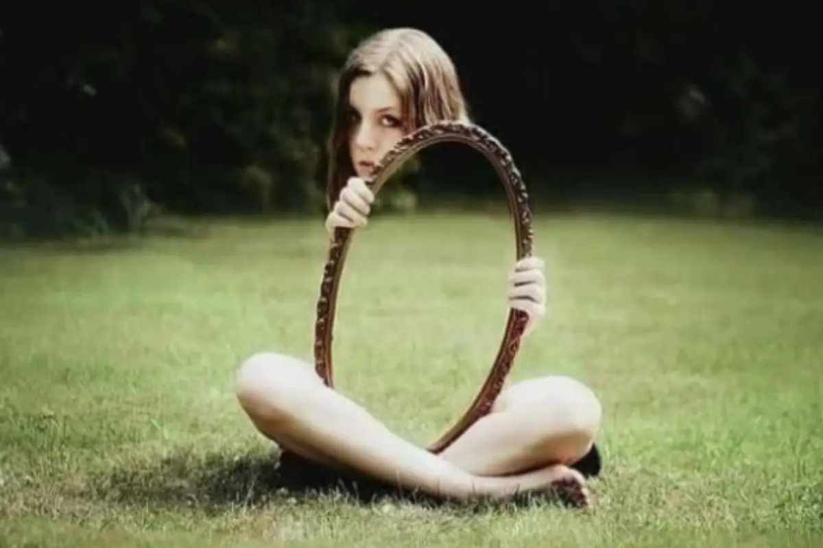 una joven sentada en el suelo sostiene un espejo que refleja el pasto