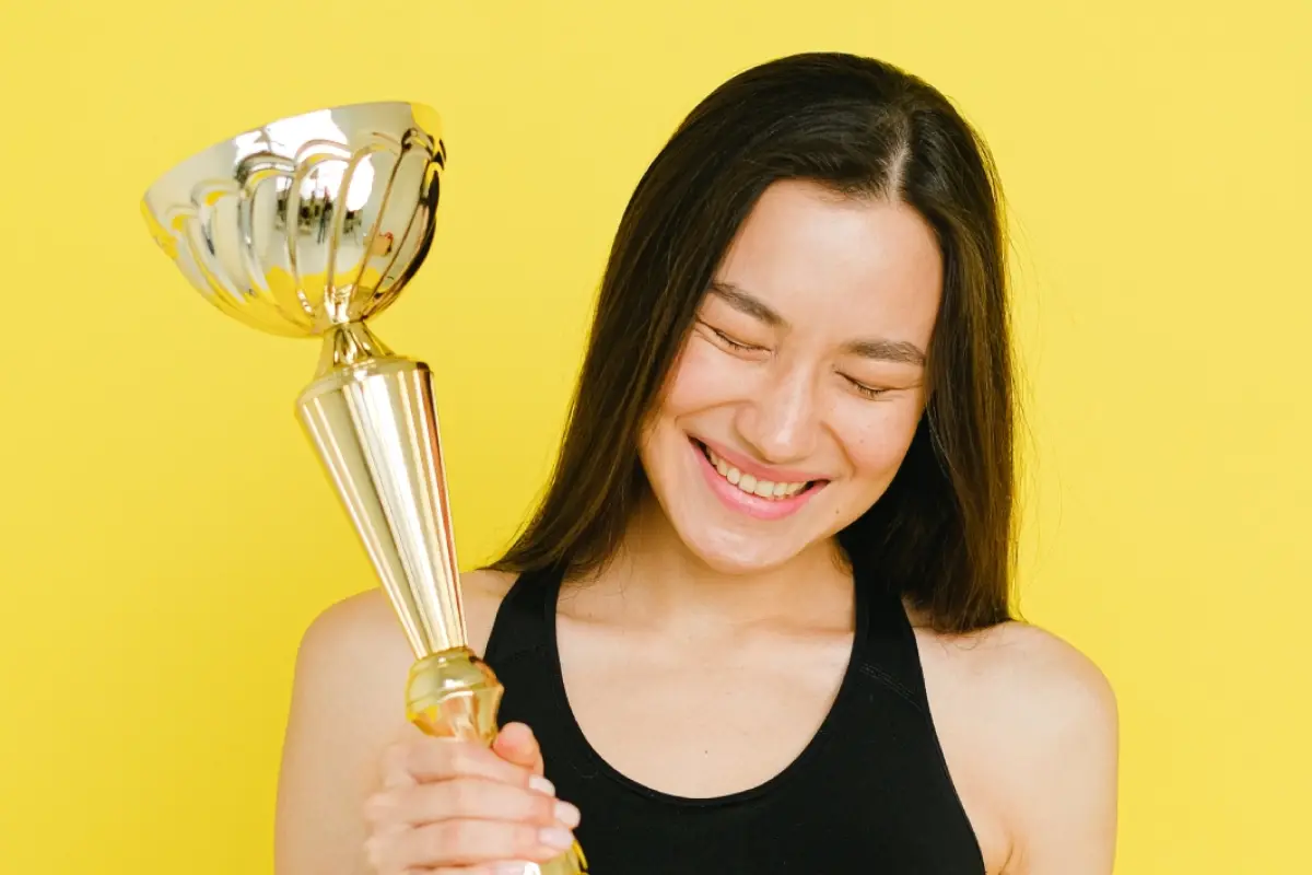 Una mujer sonríe mientras muestra orgullosa y con éxito una copa de primer lugar