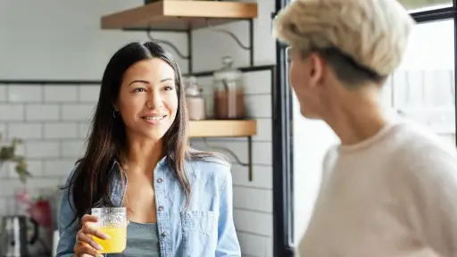 Woman Talking with Girlfriend While Holding Juice, Smiling young woman talking with girlfriend while holding juice. couple is spending leisure time at home. They are wearing casuals.