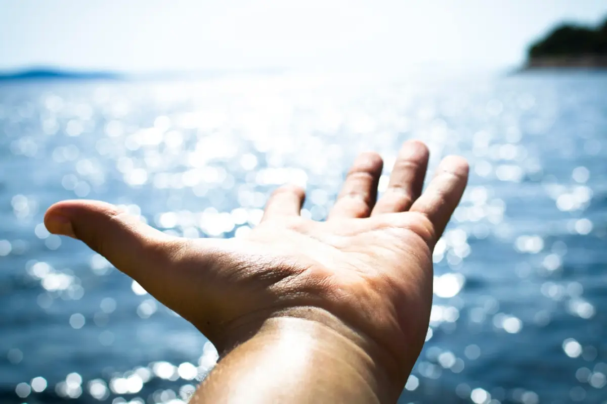 una mano con la palma hacia arriba que apunta hacia el mar en una playa, 