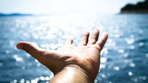 una mano con la palma hacia arriba que apunta hacia el mar en una playa, 