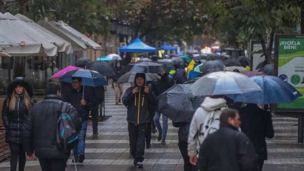 personas con paraguas caminan bajo la lluvia en una calle de santiago de chile durante las inundaciones / 
