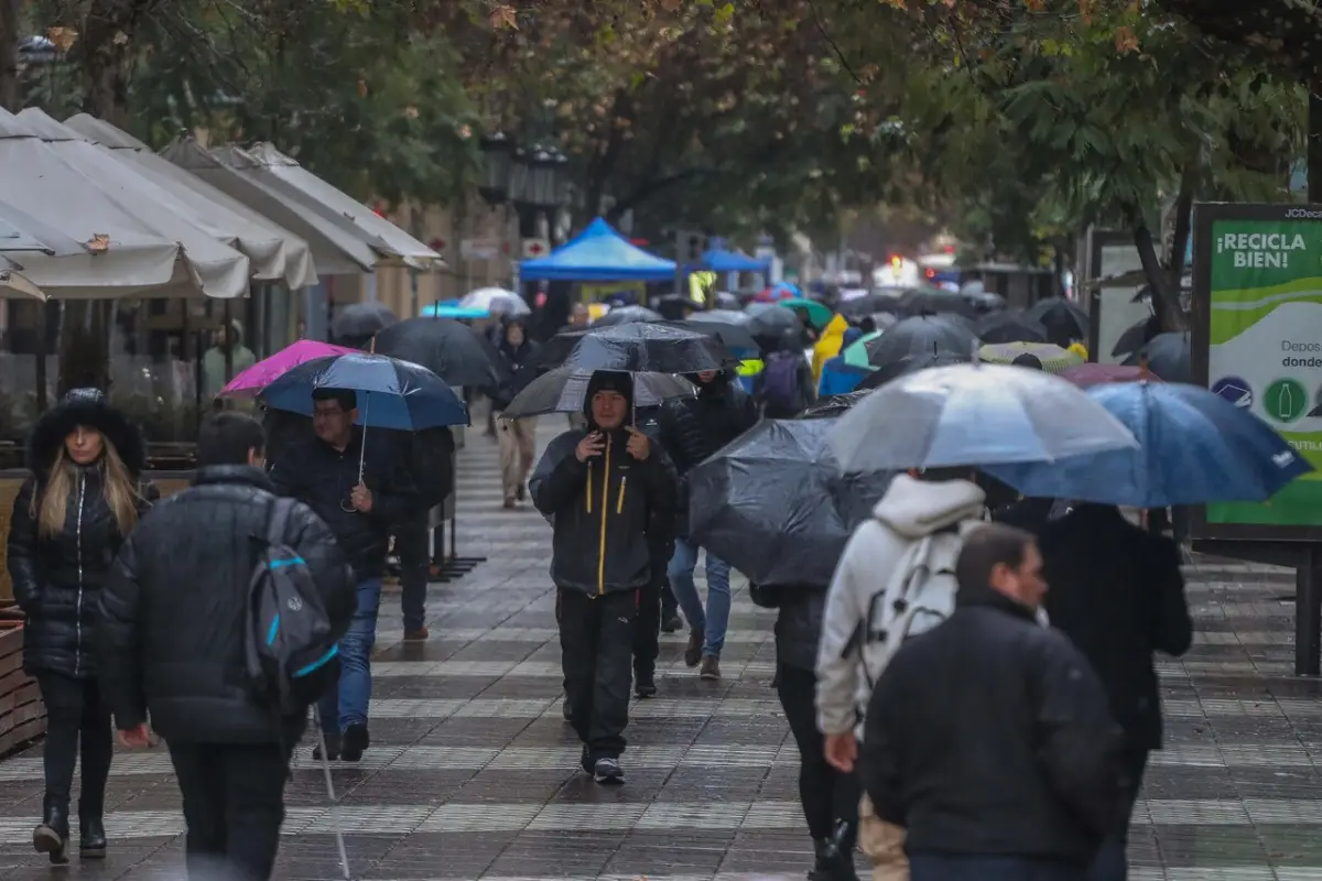 personas con paraguas caminan bajo la lluvia en una calle de santiago de chile durante las inundaciones
