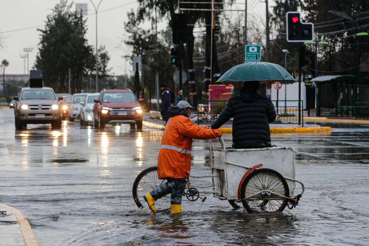 un hombre en un tricilcio ayuda a cruzar a otro en una calle inundada de santiago de chile por inundaciones / Agencia Uno
