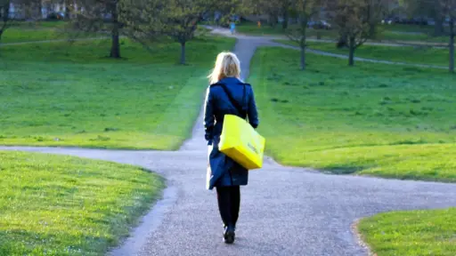 una mujer vestida de negro caminando, llega a una bifurcación de caminos
