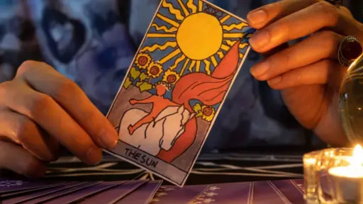 manos sosteniendo una carta del tarot sobre una mesa con velas y un mazo