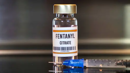 Fentanyl drug and syringe on black table with reflections and stainless background.,  