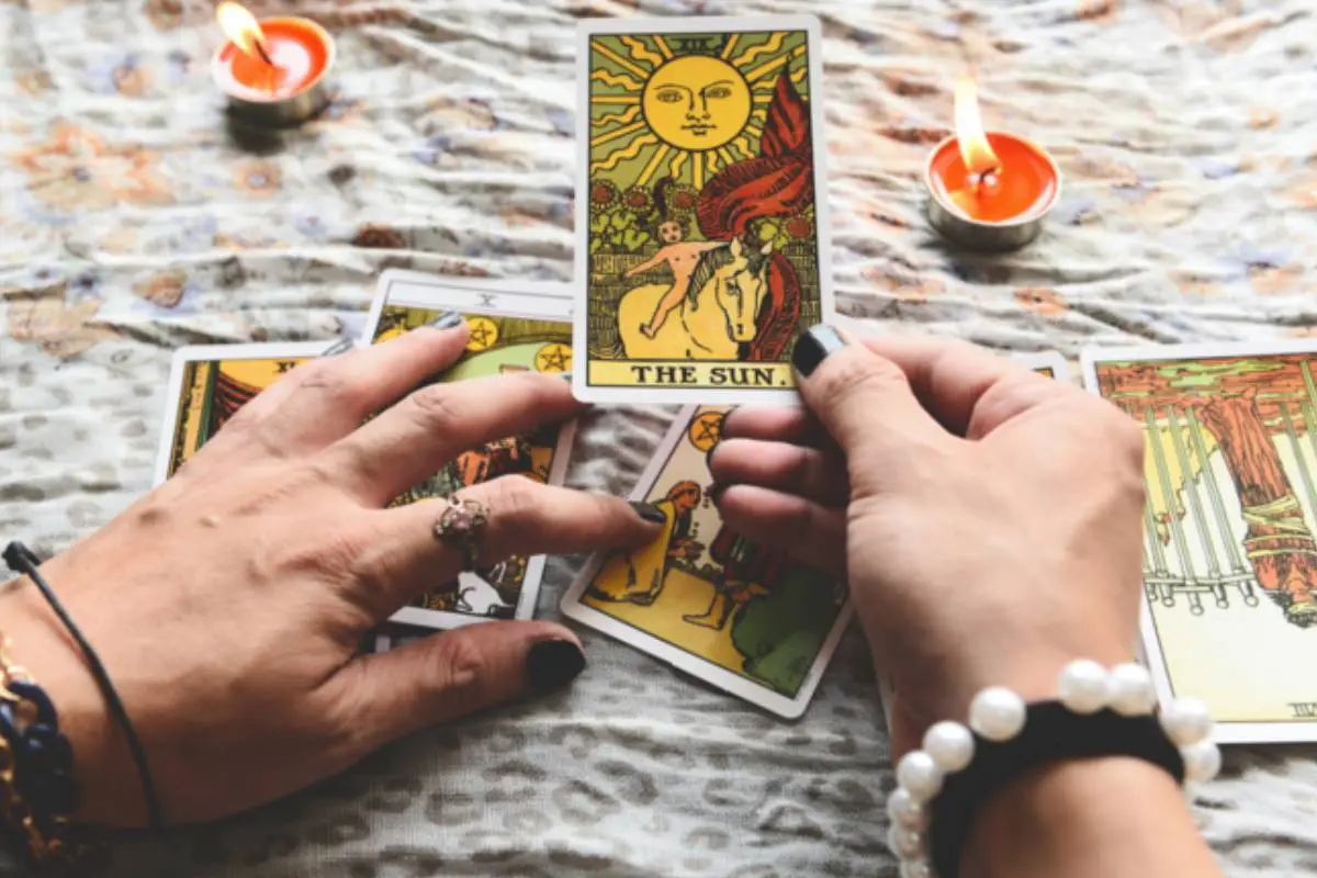 manos de mujer lanzando el tarot sobre una mesa con velas